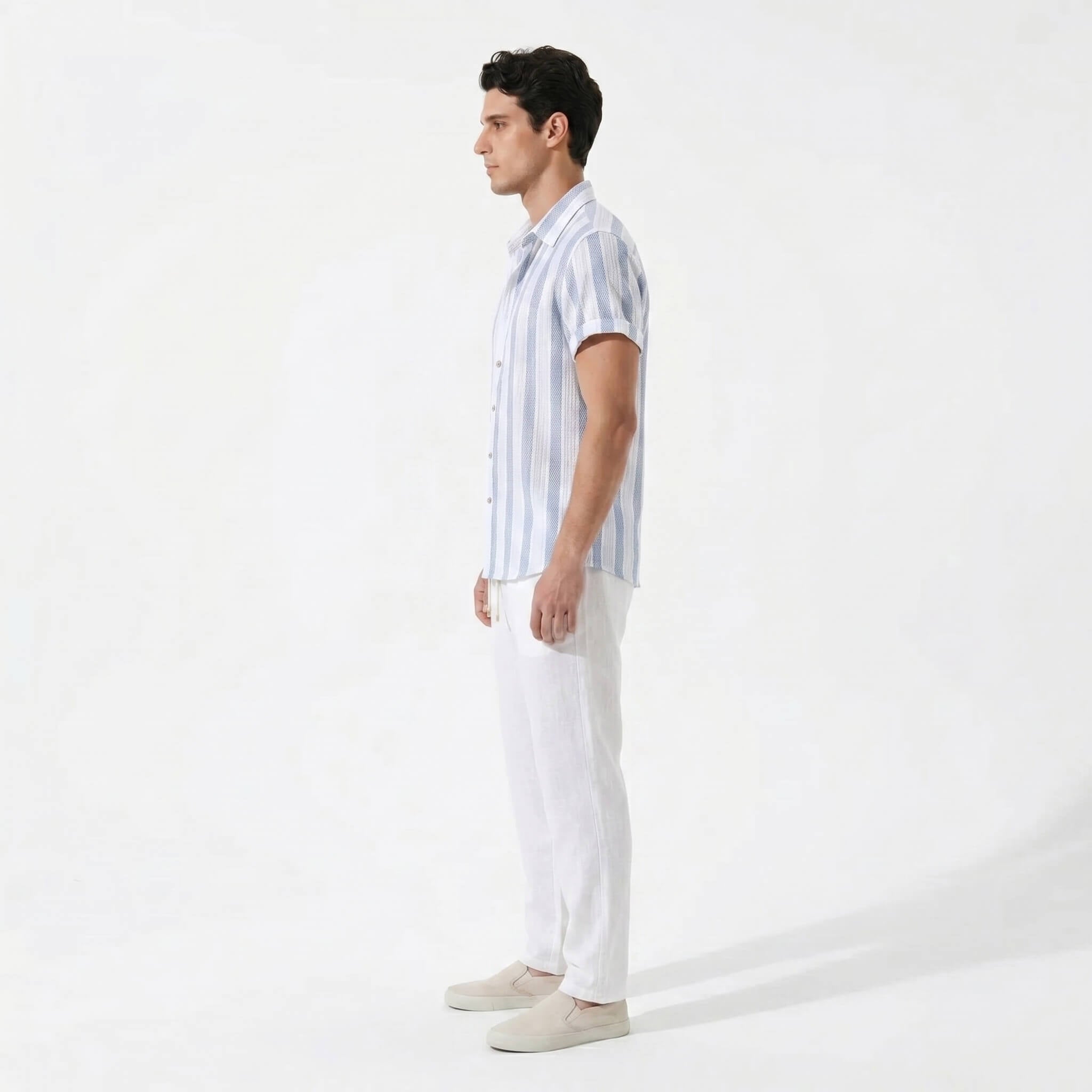 Side view of man wearing a light blue striped shirt and white pants on a white background