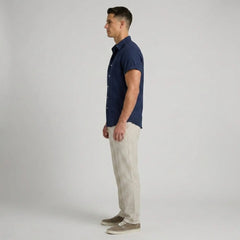 Side view of man wearing a navy button-up shirt and beige pants on a plain background
