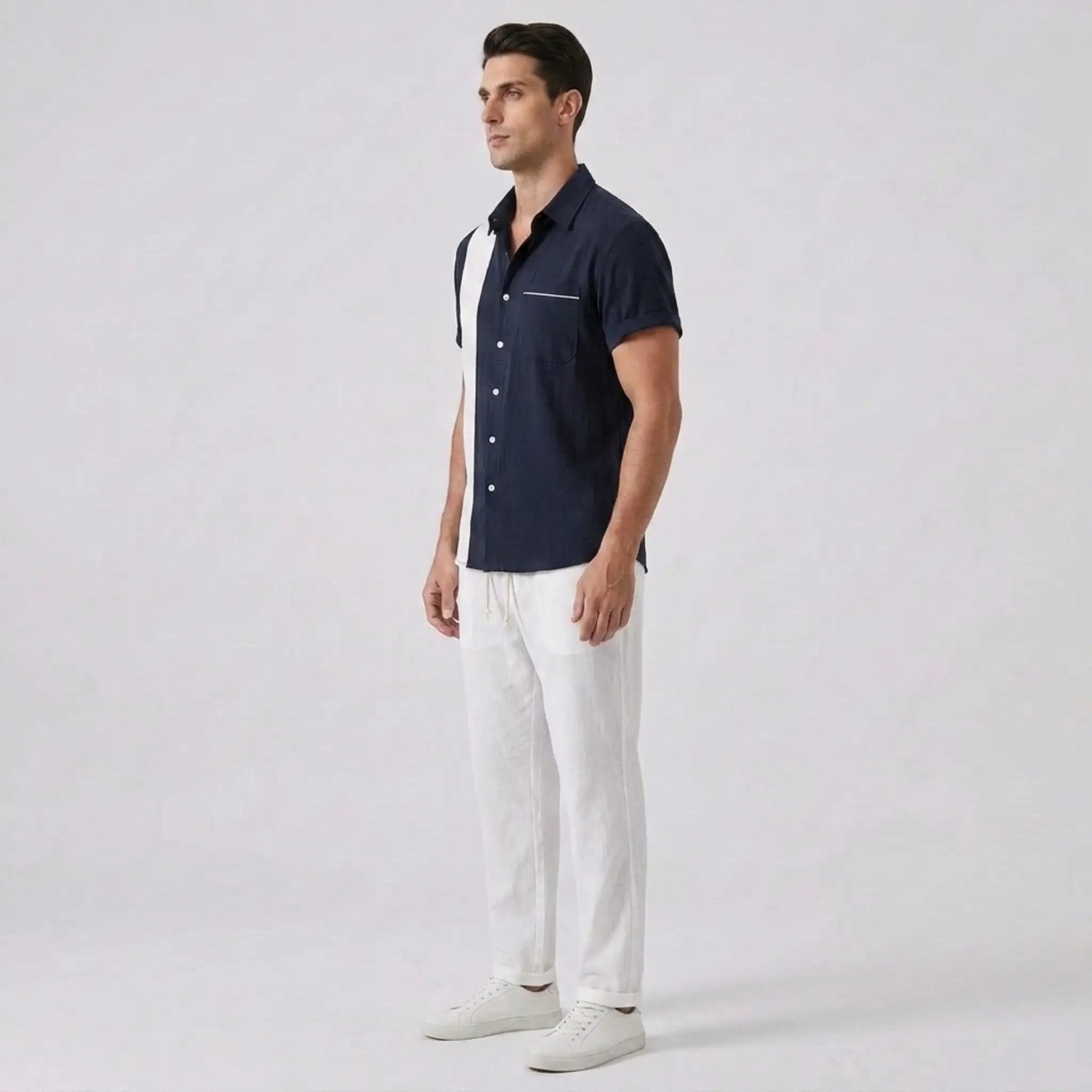 Side view of man wearing a navy button-up shirt and white pants on a light gray background