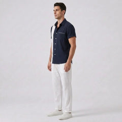 Side view of man wearing a navy button-up shirt and white pants on a light gray background