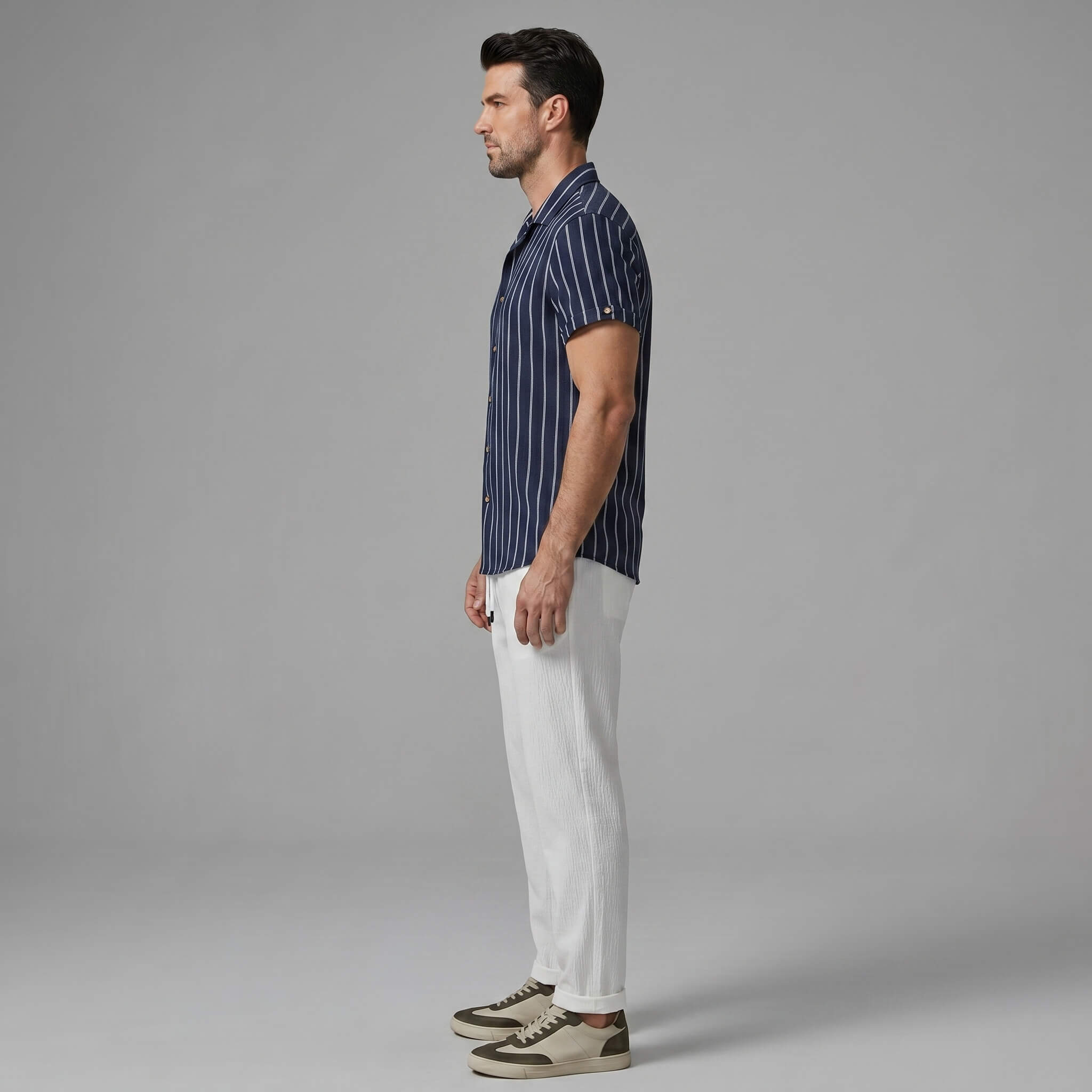 Side view of man wearing a navy striped shirt and white pants on a gray background