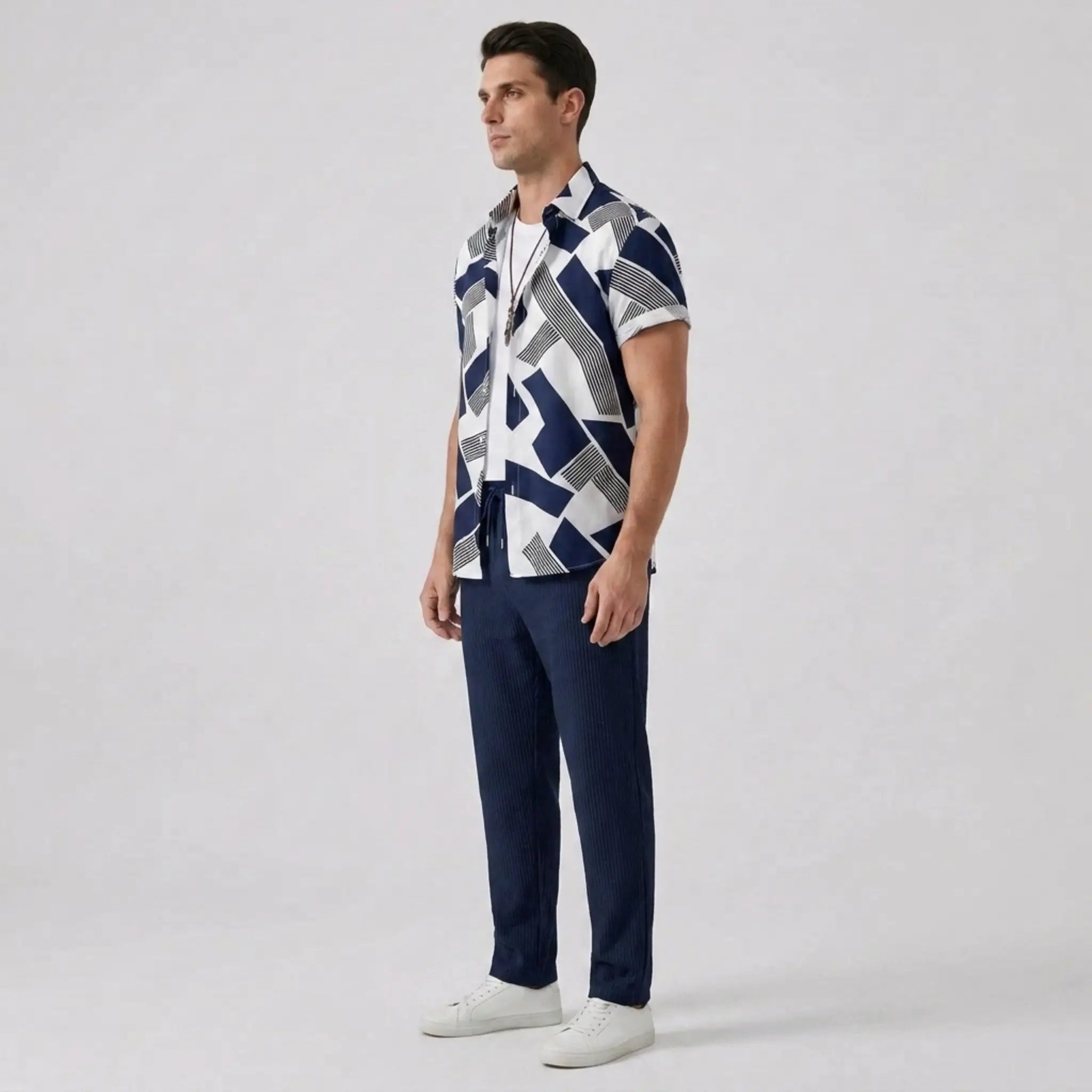 Side view of man wearing a patterned shirt and navy pants on a light gray background