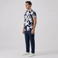 Side view of man wearing a patterned shirt and navy pants on a light gray background