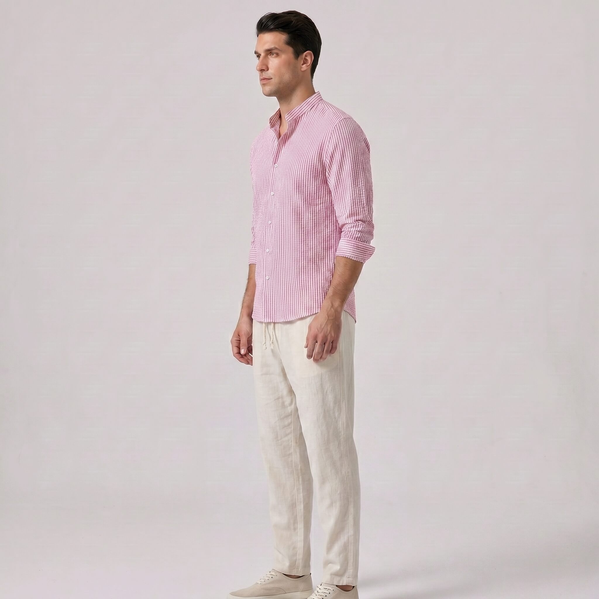 Side view of man wearing a pink checkered shirt and white pants on a light gray background