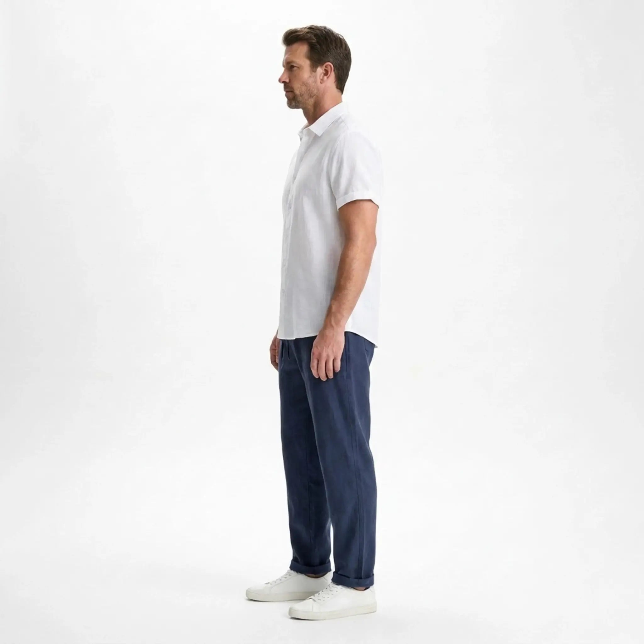 Side view of man wearing a white shirt and navy pants on a white background