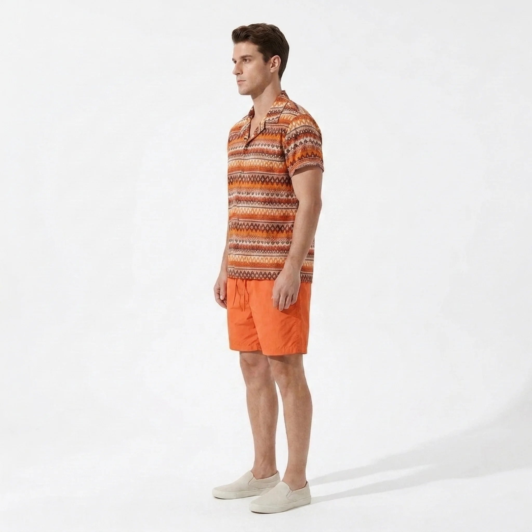 Side view of man wearing an orange patterned shirt and orange shorts on a white background