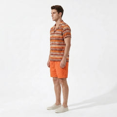 Side view of man wearing an orange patterned shirt and orange shorts on a white background