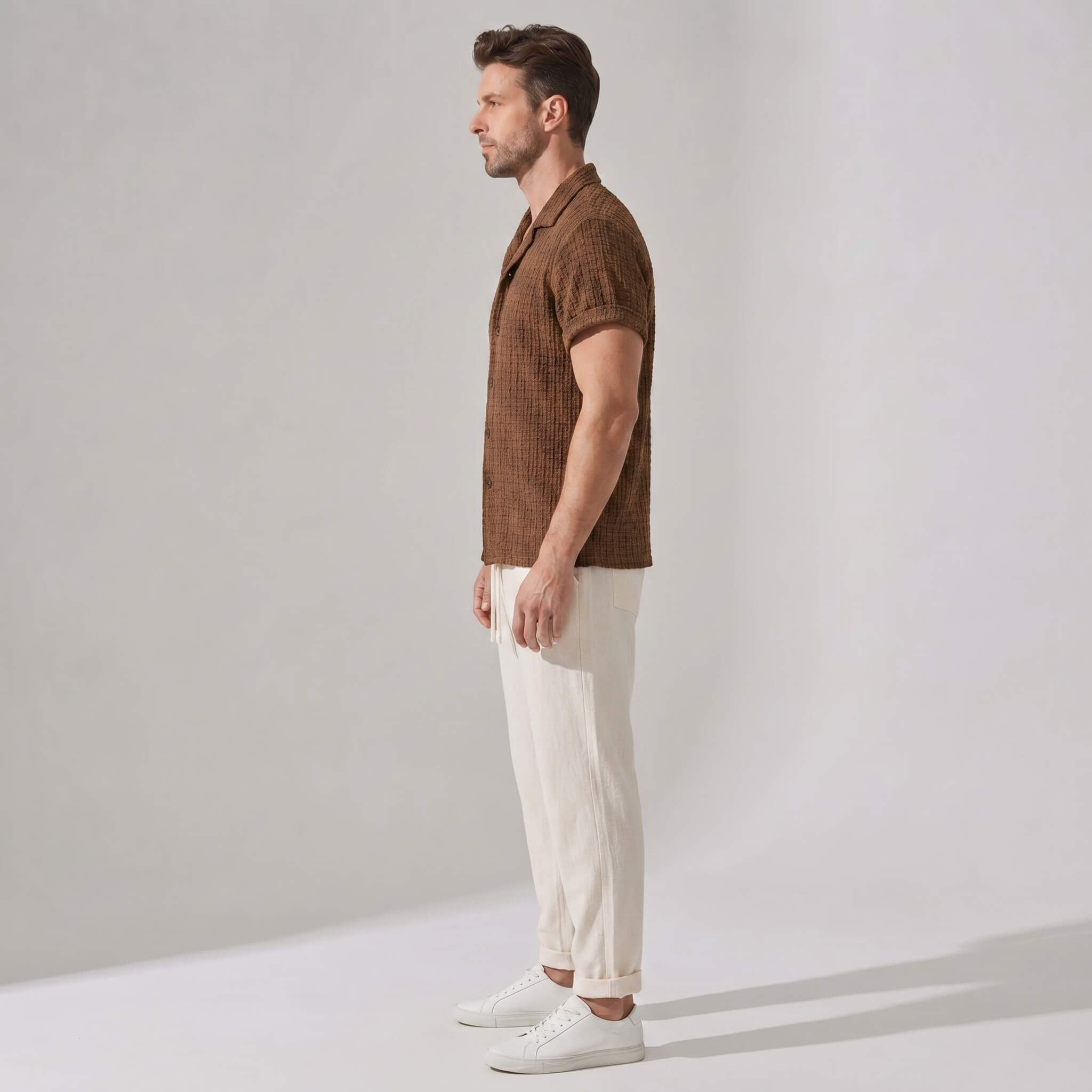 Side view of man wearing a brown patterned shirt and beige pants against a plain background