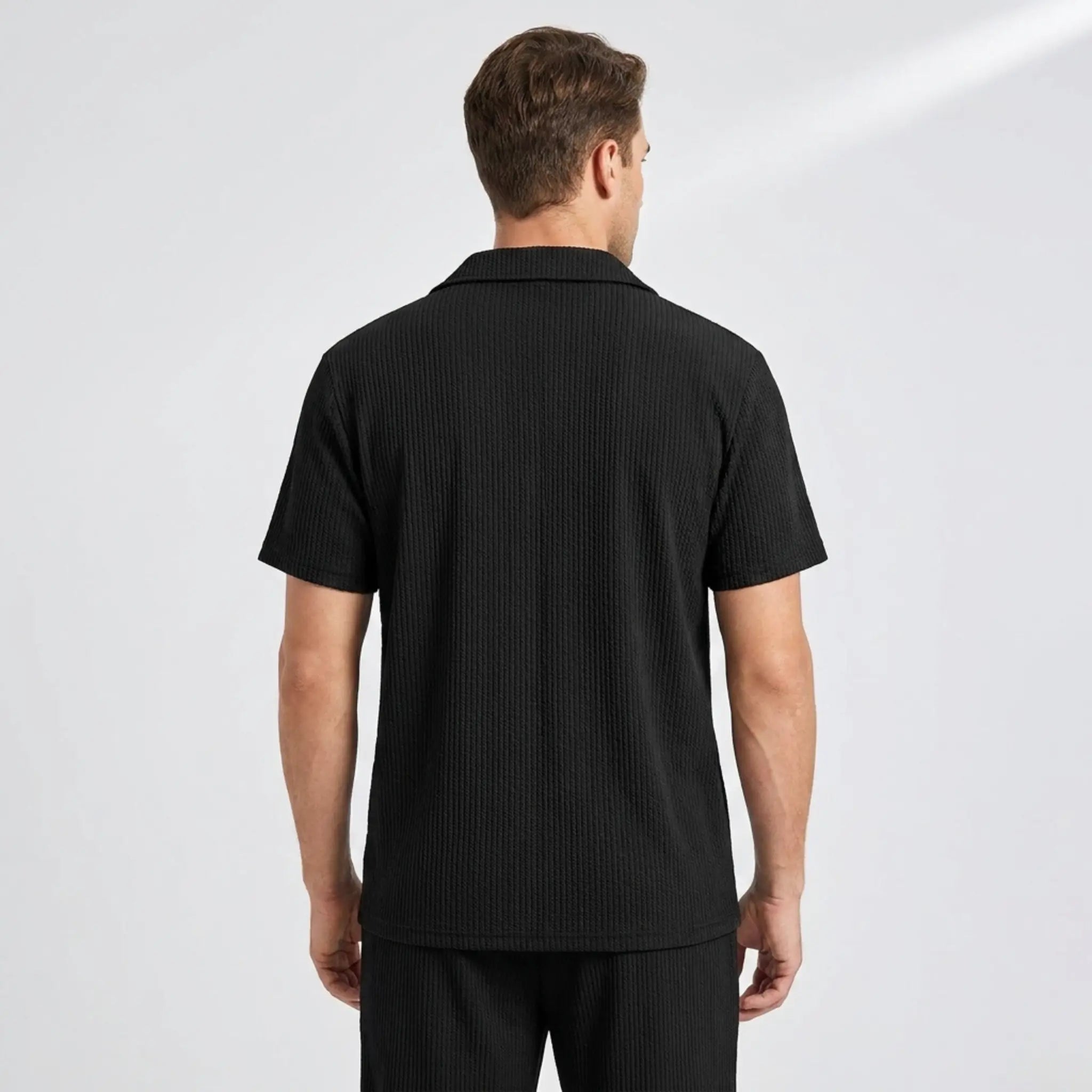 back view of man wearing a black polo shirt and trouser on a gray background