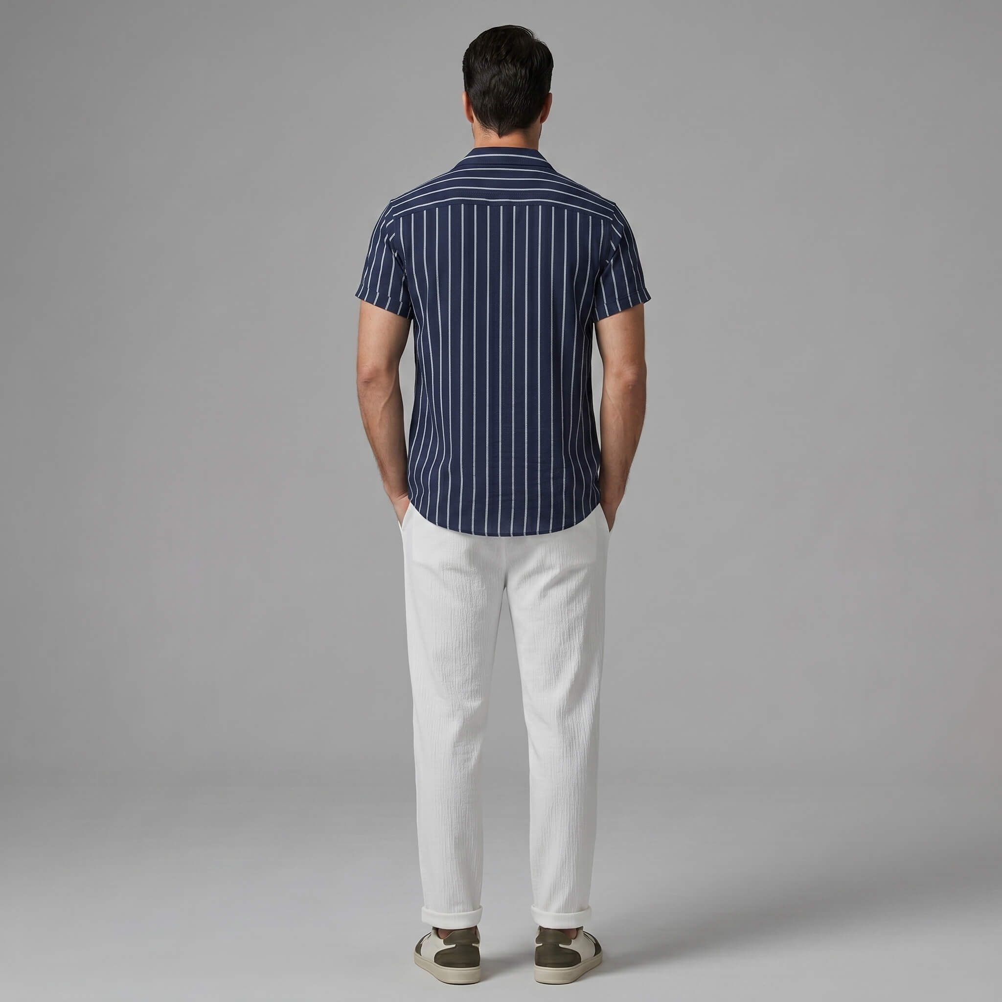 back view of man wearing a navy striped shirt and white pants on a gray background