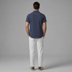 back view of man wearing a navy striped shirt and white pants on a gray background