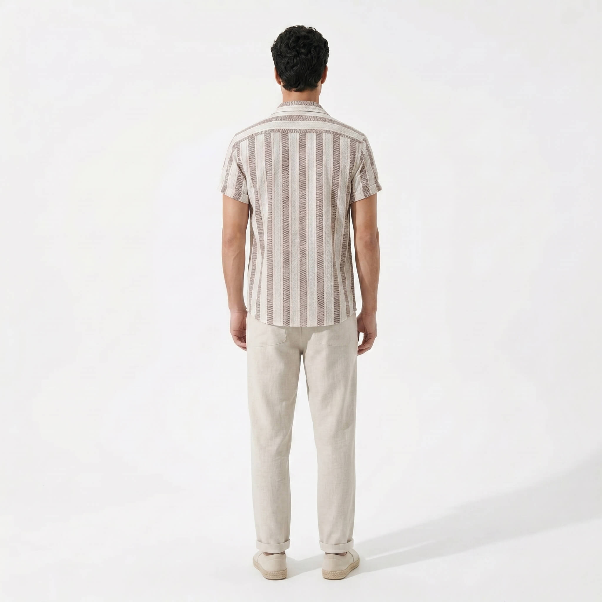 back view of man wearing a striped shirt and beige pants on a white background