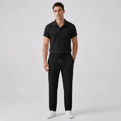 Man wearing a black polo shirt and pants with white shoes front view on a light gray background