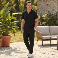 man wearing a black polo shirt and trouser walking on stoned floor in a garden lifestyle view