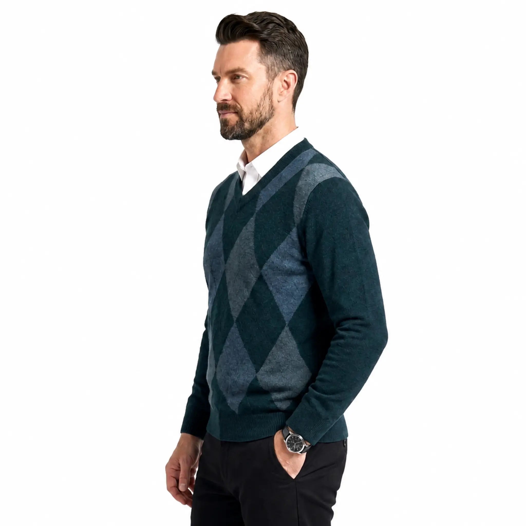 A man wearing a dark teal and green argyle sweater over a white collared shirt and black trousers, standing against a plain white background.