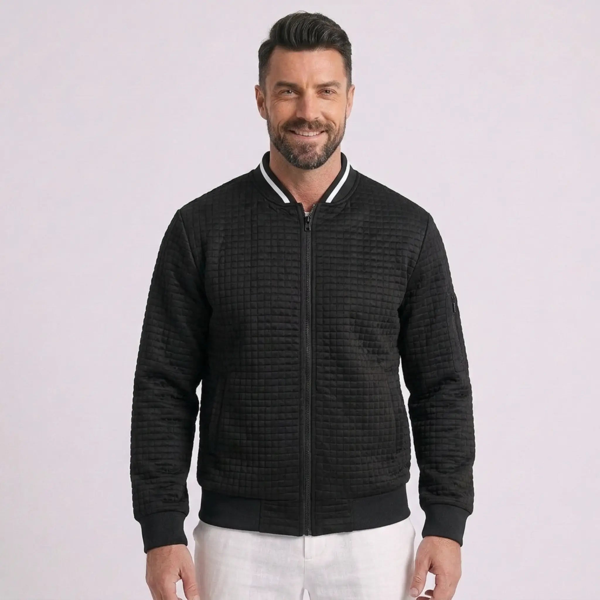 Man wearing MannerCo black quilted zip-up baseball jacket with stand collar, front view on plain background