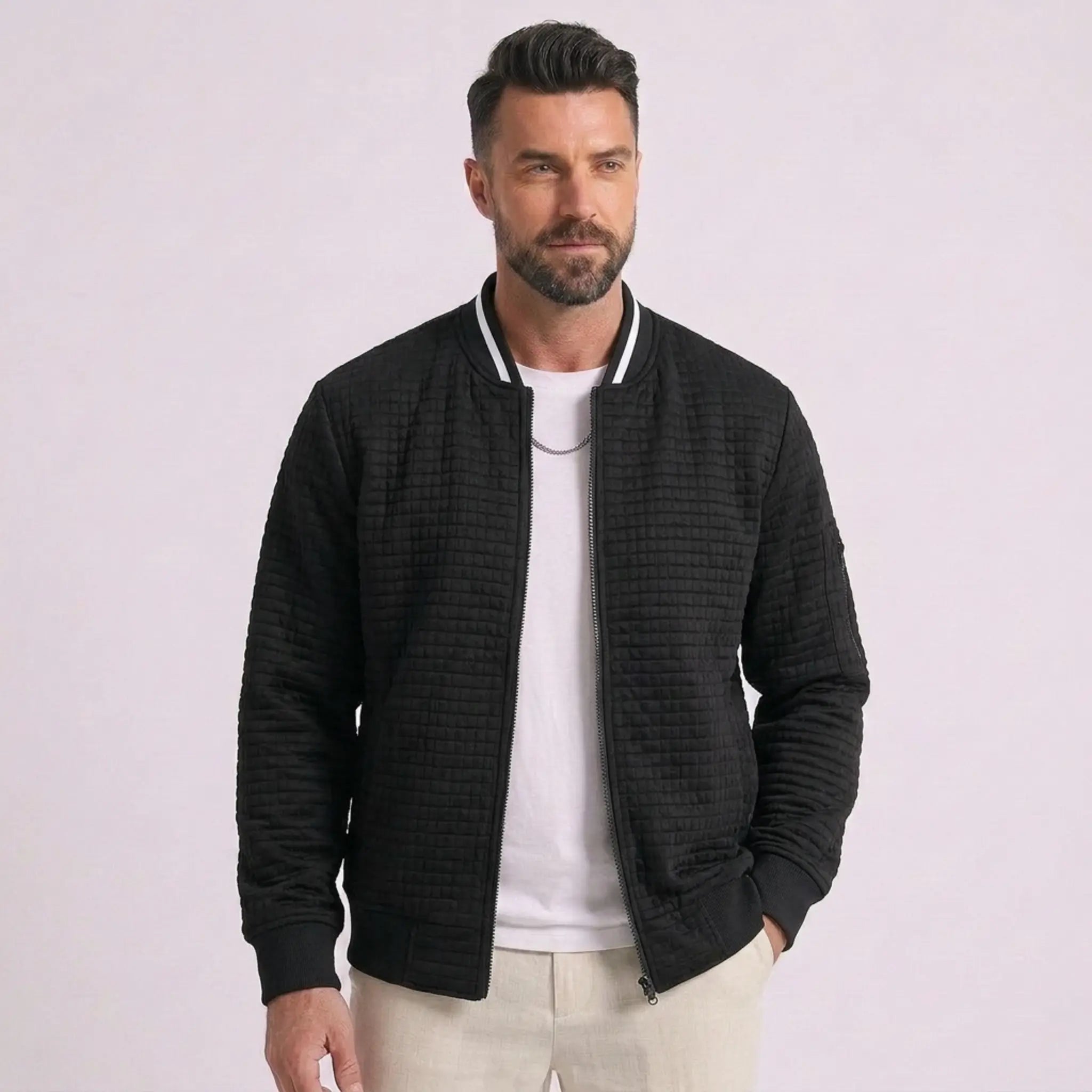 Man wearing MannerCo black quilted zip-up baseball jacket with stand collar, front view