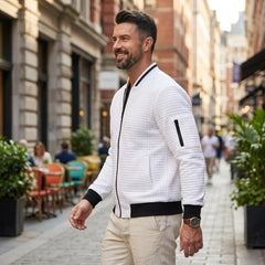 Man wearing MannerCo white quilted zip-up baseball jacket in outdoor lifestyle setting