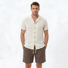 Back view of man wearing beige floral checkerboard jacquard Cuban shirt and linen drawstring shorts