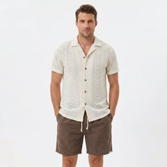 Back view of man wearing beige floral checkerboard jacquard Cuban shirt and linen drawstring shorts