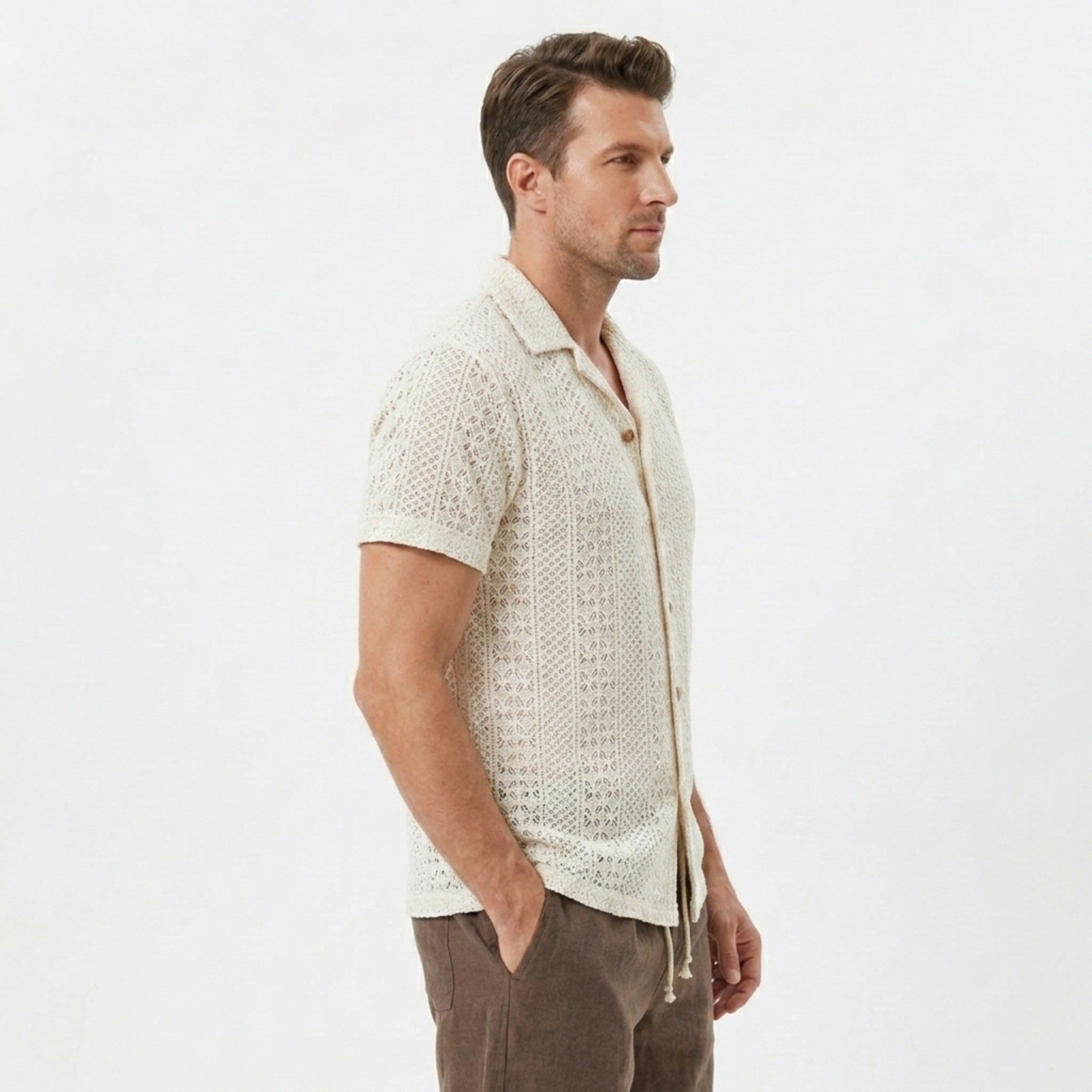 Side view of man in beige floral checkerboard jacquard Cuban shirt and linen drawstring shorts