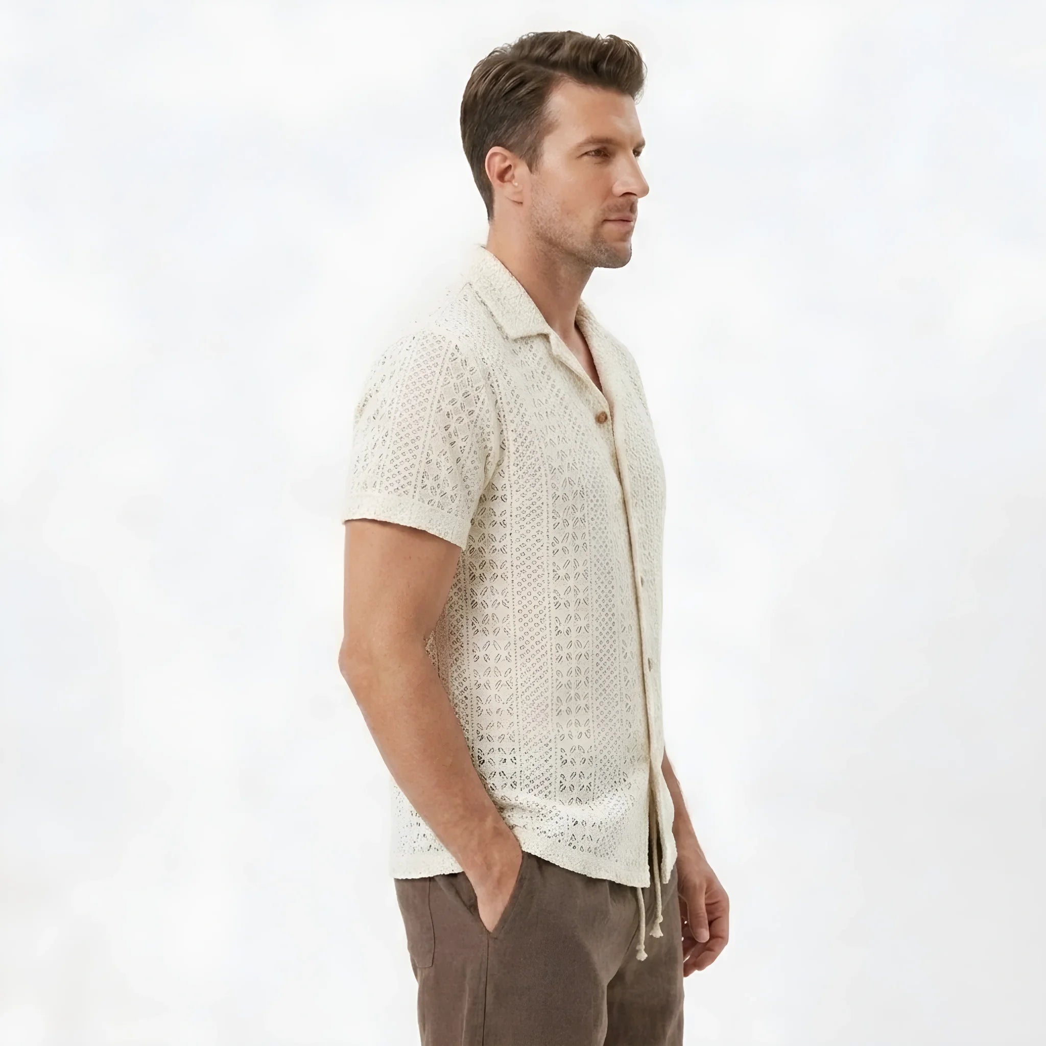 Side view of man in beige floral checkerboard jacquard Cuban shirt and linen drawstring shorts