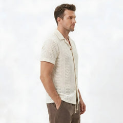 Side view of man in beige floral checkerboard jacquard Cuban shirt and linen drawstring shorts