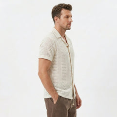 Side view of man in beige floral checkerboard jacquard Cuban shirt and linen drawstring shorts