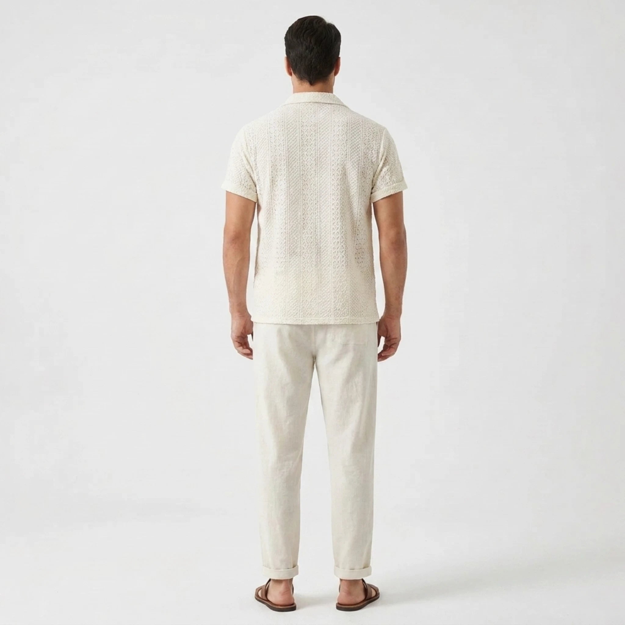 Back view of man wearing beige floral checkerboard jacquard Cuban shirt and straight leg linen pants
