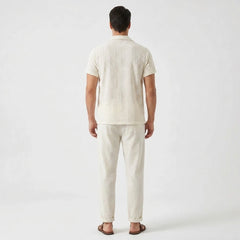 Back view of man wearing beige floral checkerboard jacquard Cuban shirt and straight leg linen pants