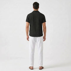 Man wearing beige floral checkerboard jacquard Cuban shirt and linen pants in resort setting