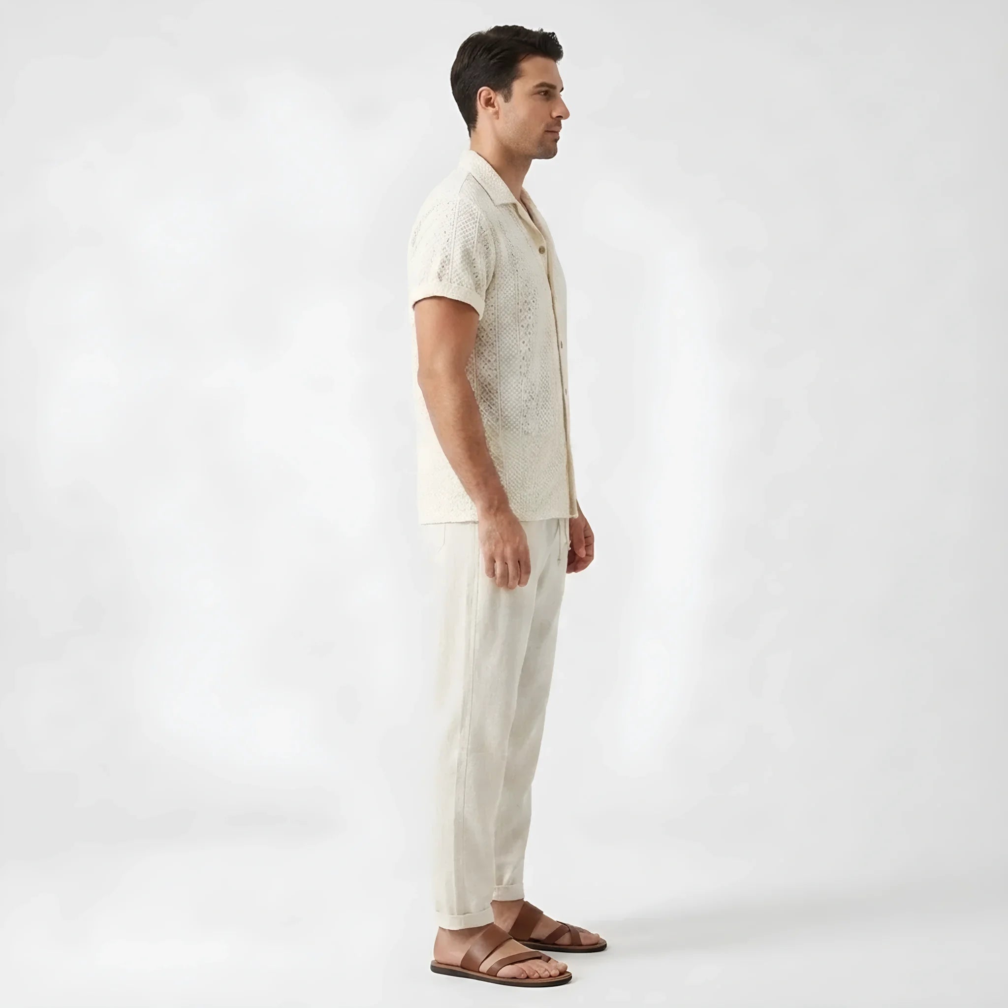 Side view of man in beige floral checkerboard jacquard Cuban shirt and straight leg linen pants