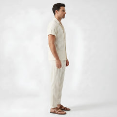 Side view of man in beige floral checkerboard jacquard Cuban shirt and straight leg linen pants