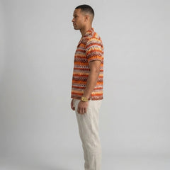 Side view of man in beige geometric Cuban shirt and straight leg linen pants on plain background
