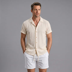 Man wearing a beige geometric jacquard button up shirt and crinkle textured shorts front view