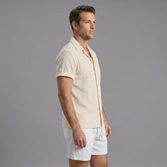 Side view of man in beige geometric jacquard shirt and crinkle shorts on plain background