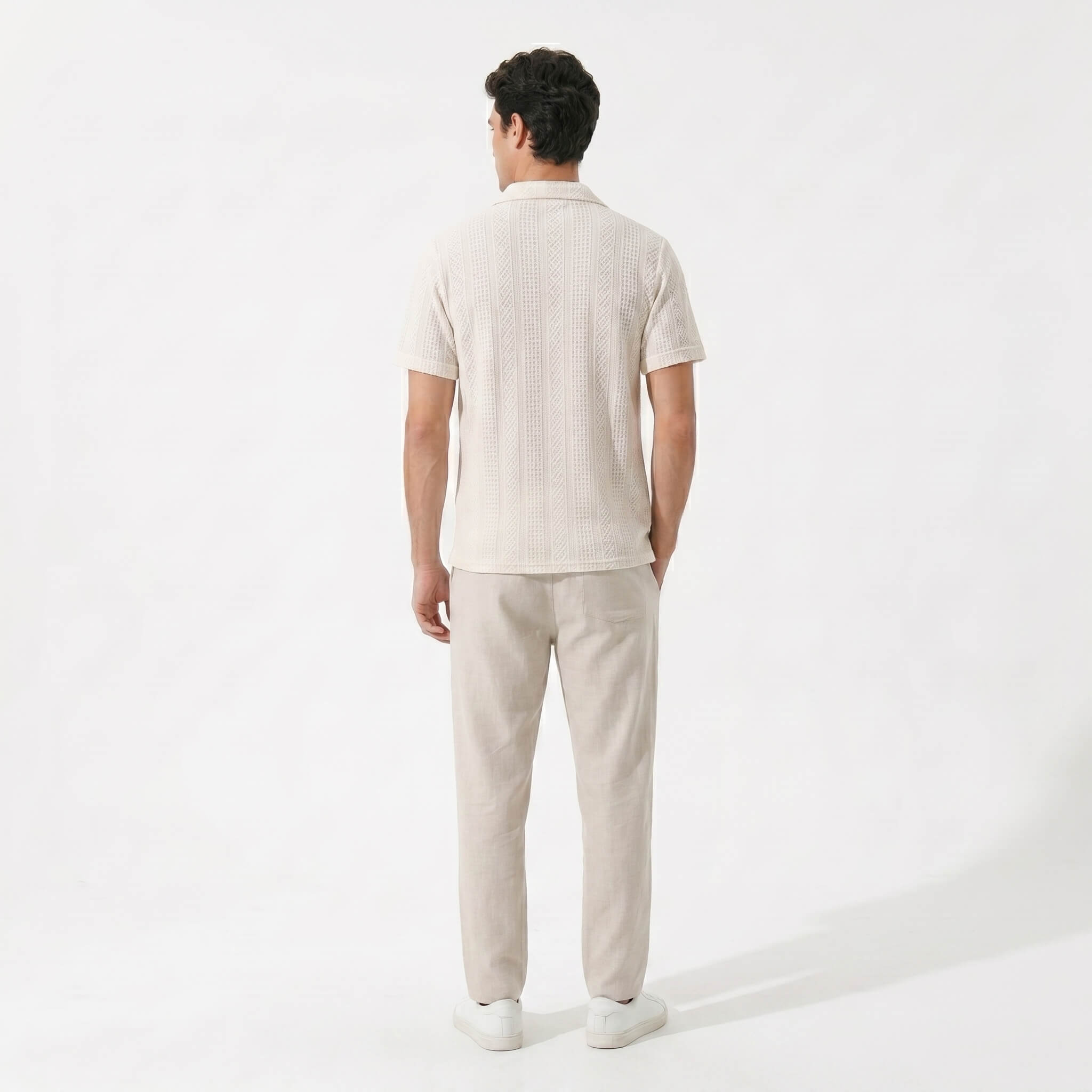 Back view of man in beige geometric jacquard shirt and linen pants on plain background