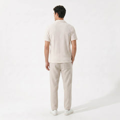 Back view of man in beige geometric jacquard shirt and linen pants on plain background