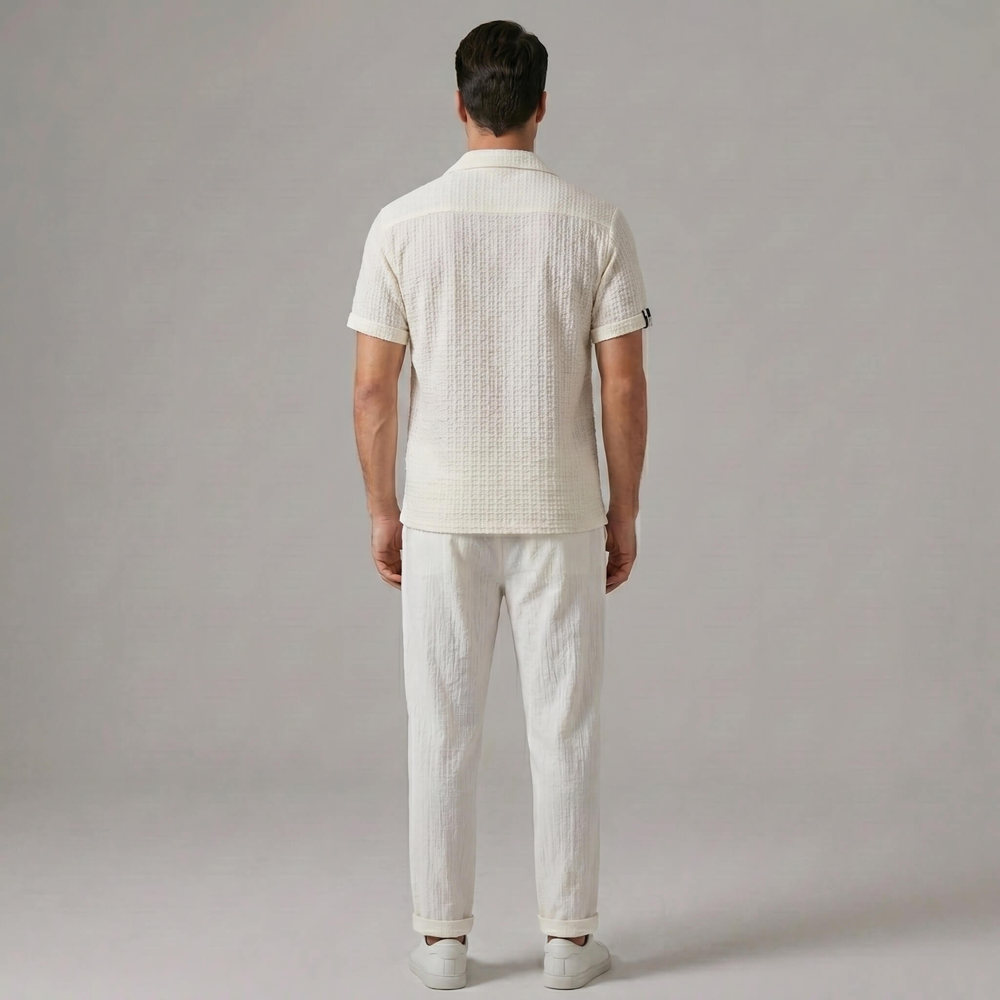 Back view of man wearing beige jacquard Cuban collar shirt and crinkle textured straight leg pants