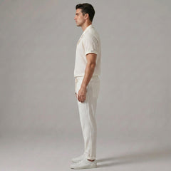 Side view of man in beige jacquard Cuban shirt and crinkle straight leg pants on plain background