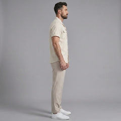 Side view of man in beige linen Cuban collar shirt and slim fit tapered trousers on plain background