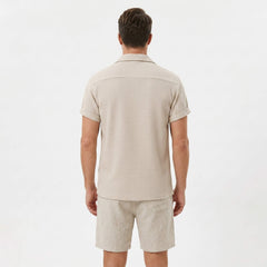 Side view of man in beige textured Cuban shirt and linen cotton drawstring shorts on plain background