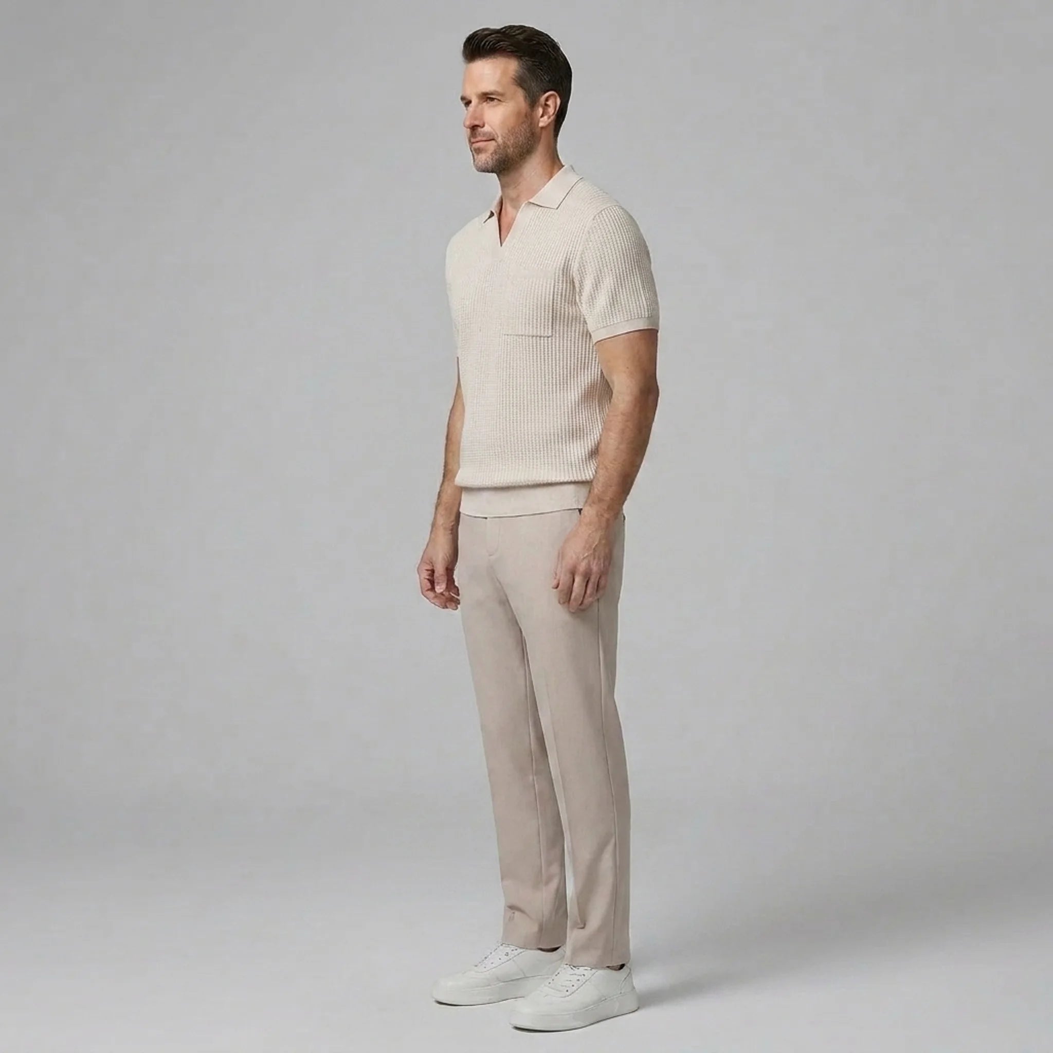 Side view of man in beige waffle johnny collar polo and slim fit tapered pants on plain background