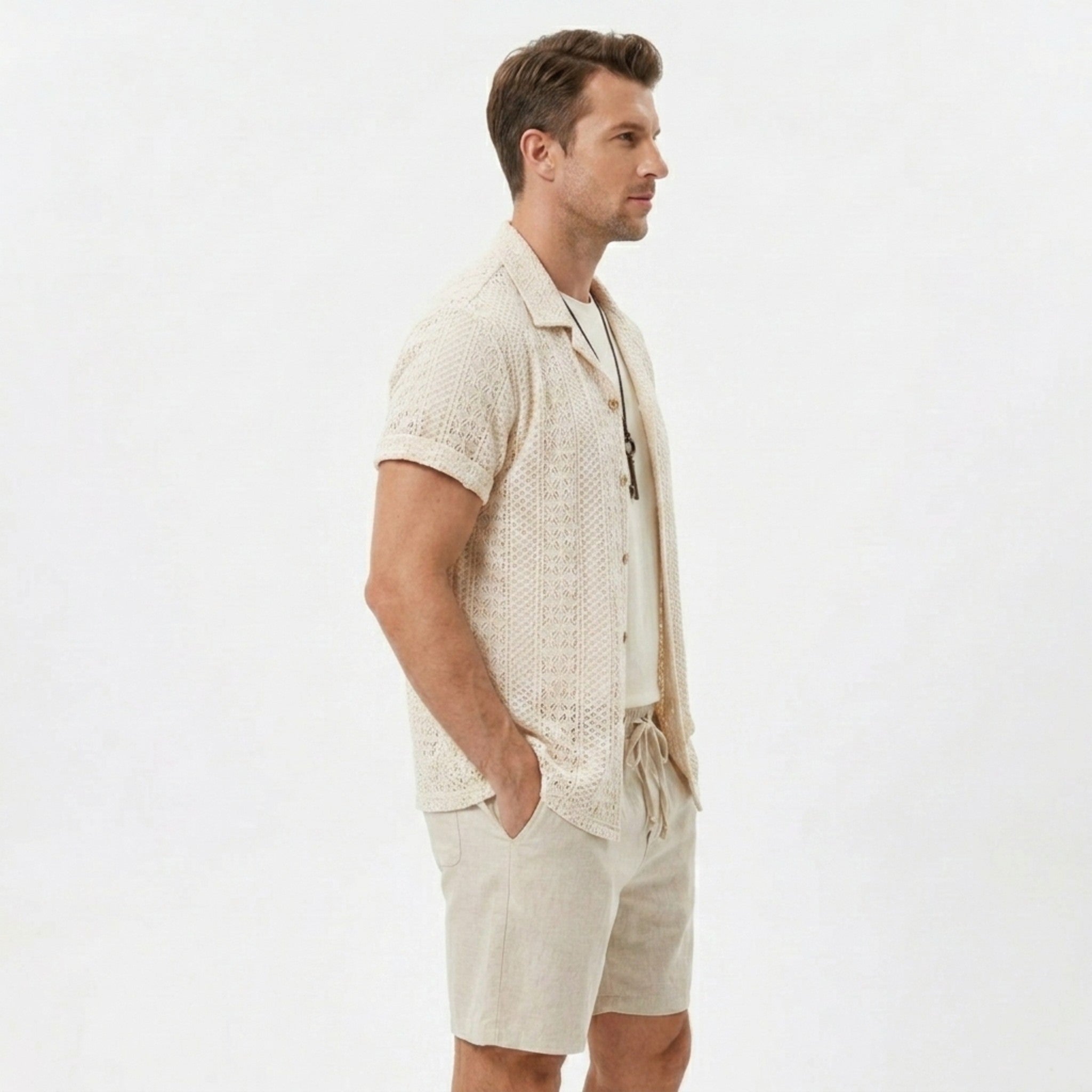 Side view of man in black floral checkerboard jacquard Cuban shirt and linen drawstring shorts