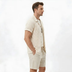 Side view of man in black floral checkerboard jacquard Cuban shirt and linen drawstring shorts