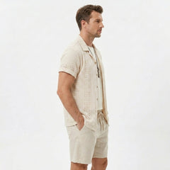 Side view of man in black floral checkerboard jacquard Cuban shirt and linen drawstring shorts