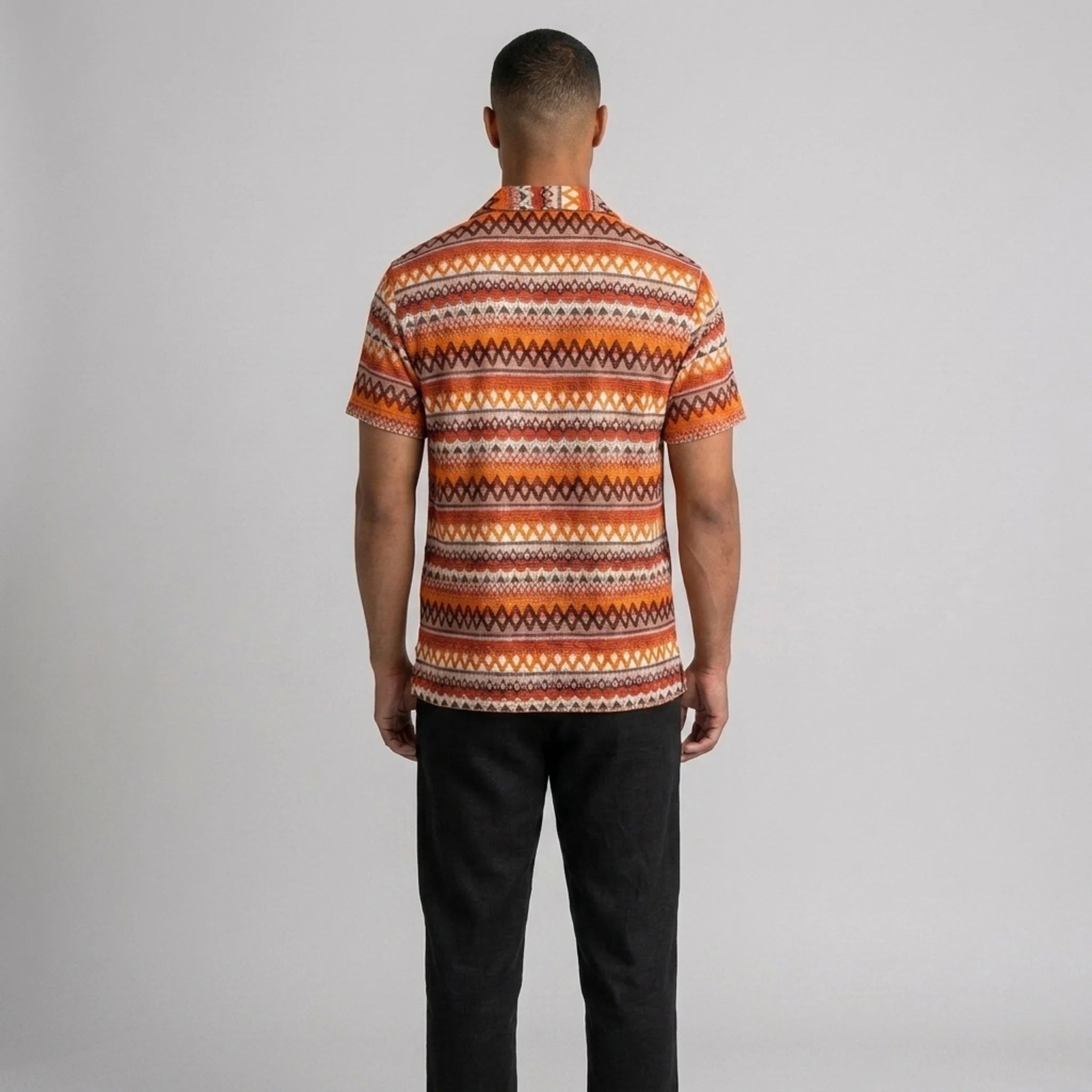 Side view of man in black geometric Cuban shirt and straight leg linen pants on plain background