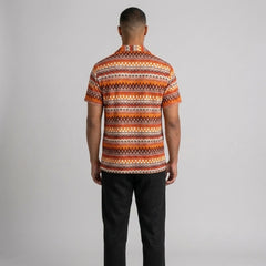 Side view of man in black geometric Cuban shirt and straight leg linen pants on plain background