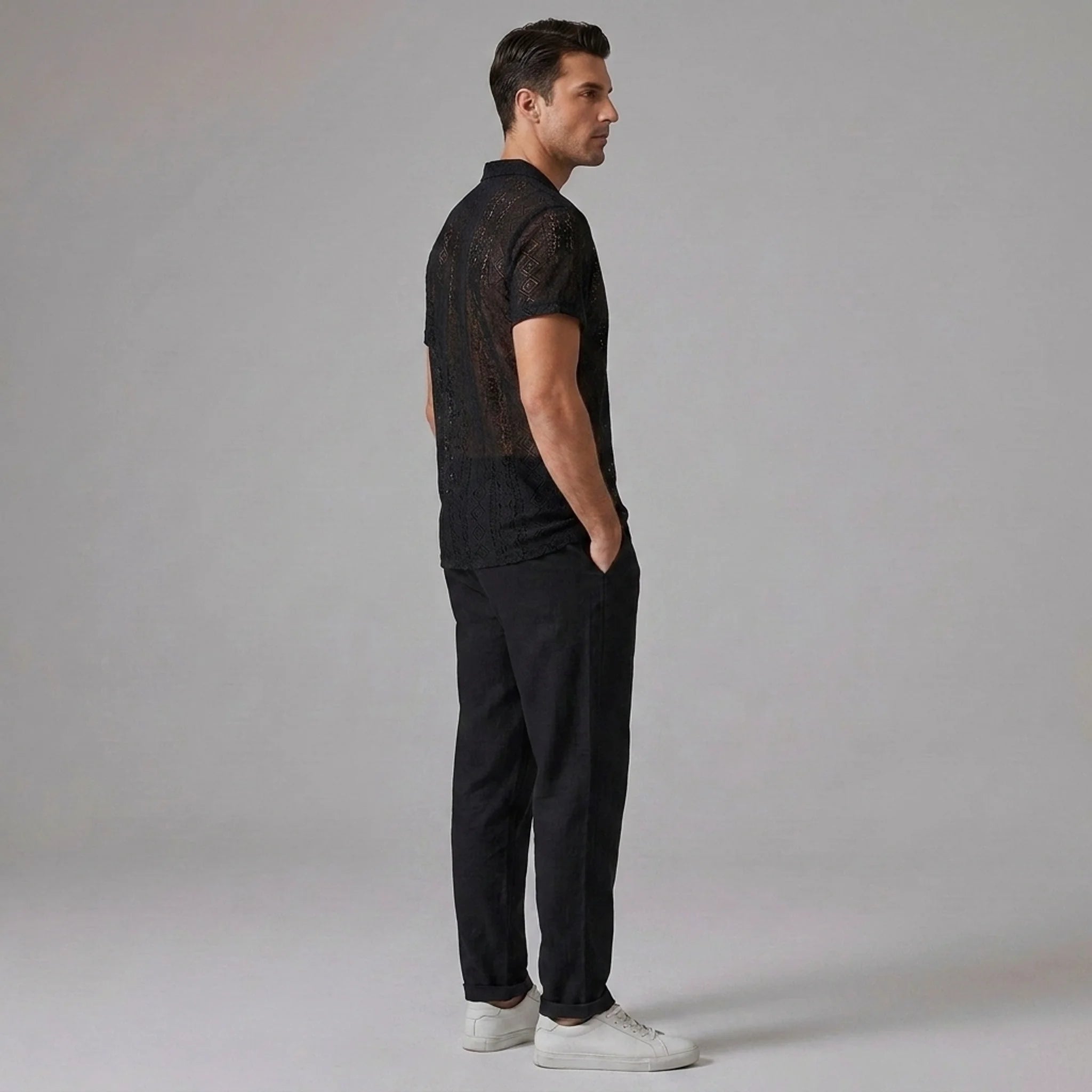 Side view of man in black geometry textured Cuban shirt and straight leg linen pants on plain background