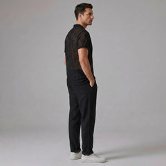 Side view of man in black geometry textured Cuban shirt and straight leg linen pants on plain background